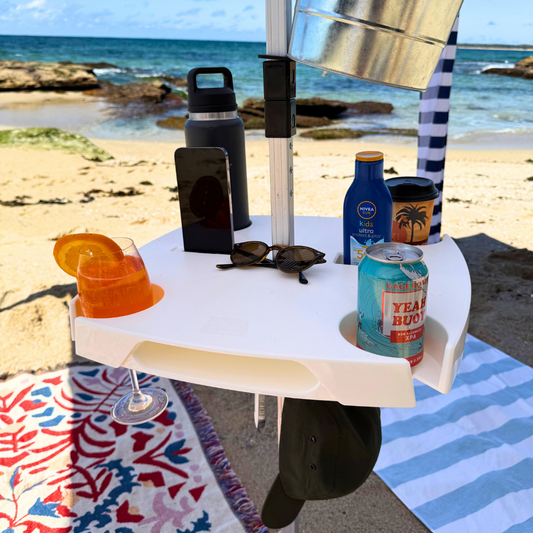 Beachside setup with a small table holding drinks, a phone, and other items on a sandy beach.