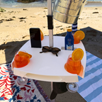 Small table with drinks, phone, and sunglasses on a beach setting