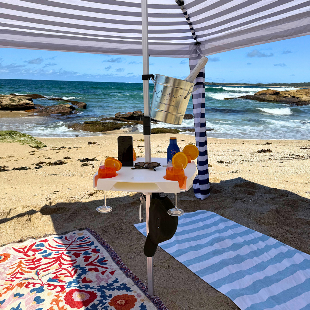 Beach setting with a striped umbrella, table, and beach towels by the ocean.