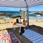 Beach setting with a striped umbrella, table, and beach towels by the ocean.