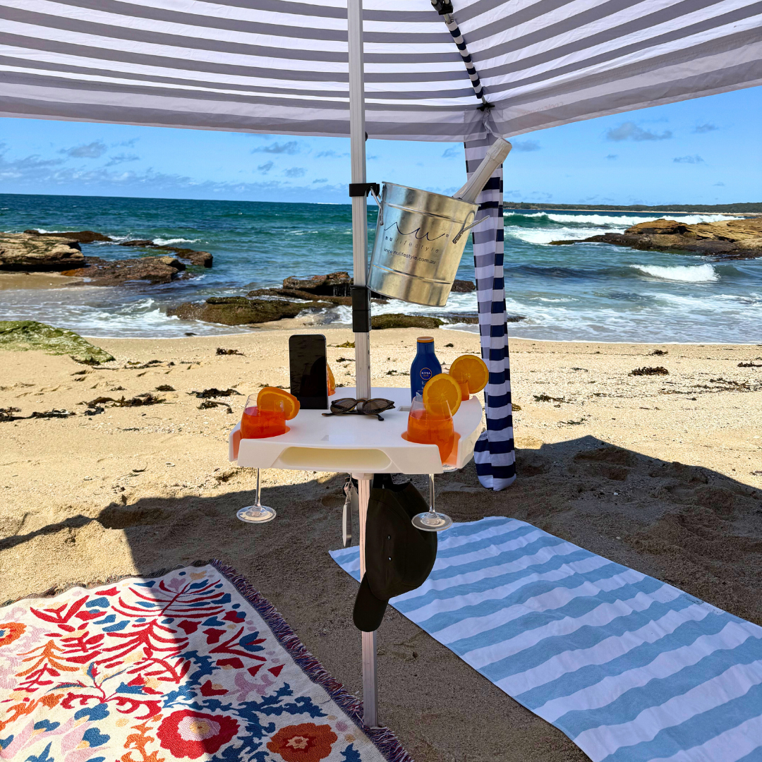 Beach setting with a striped umbrella, table, and beach towels by the ocean.